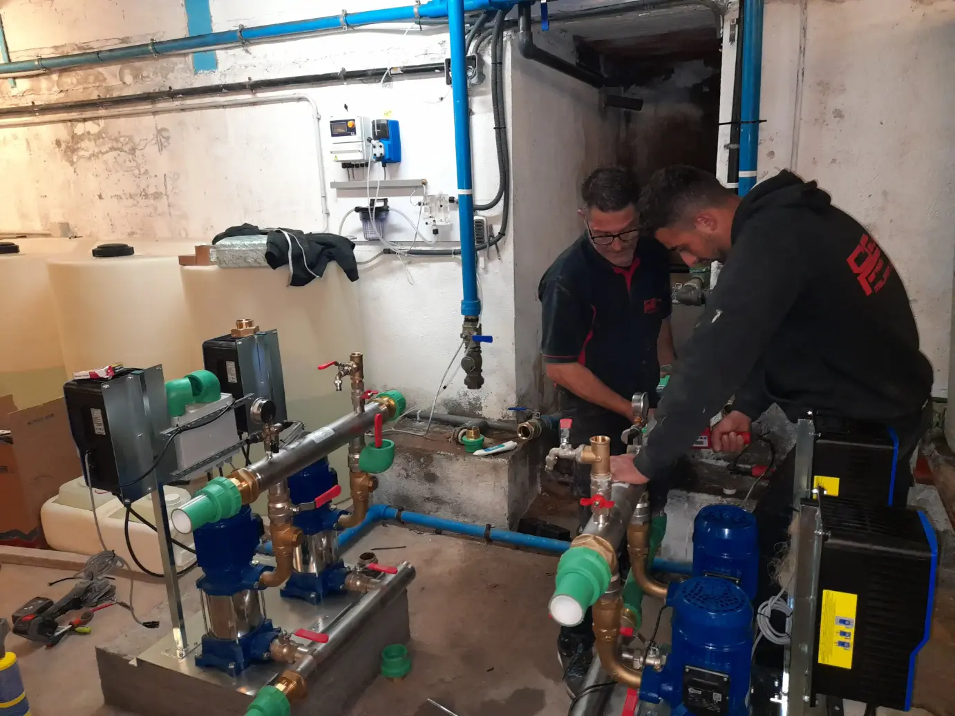 Fontaneros trabajando en la instalación de un sistema de bombeo de agua en una sala técnica de fontanería industrial.